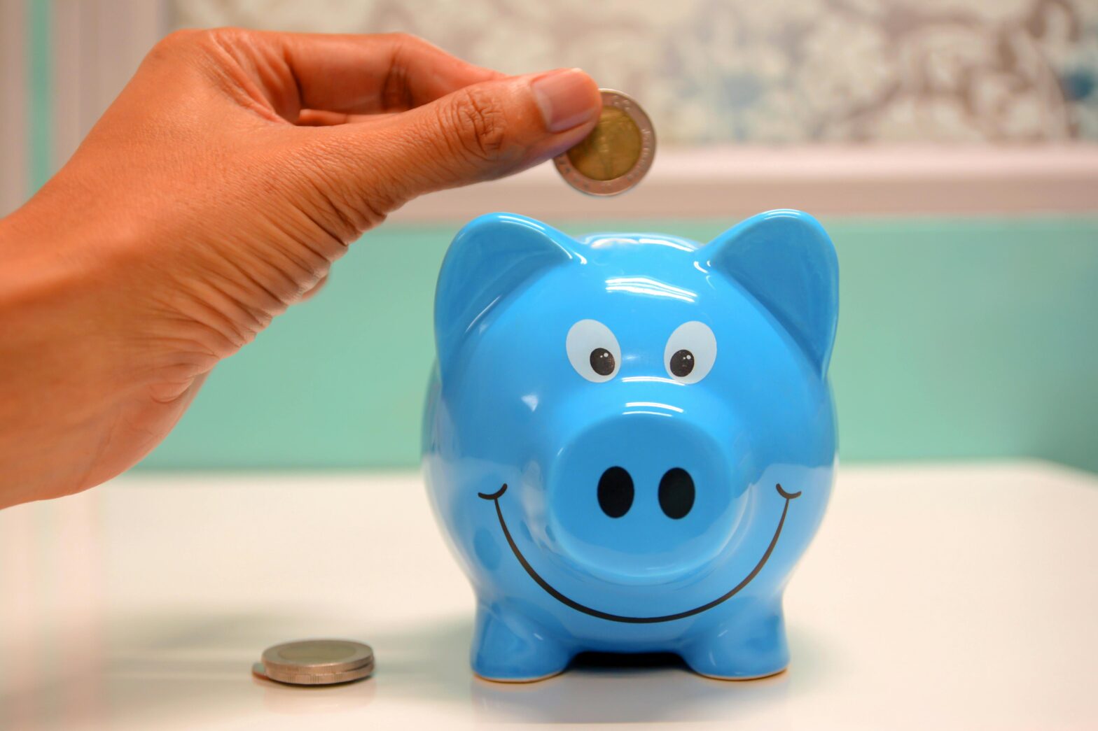 Hand putting coins into blue piggy bank.